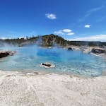 Captivating blue geyser pool in Yellowstone National Park with steam under a clear blue sky.