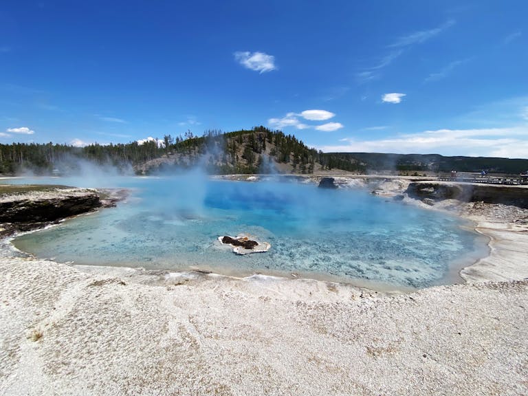Captivating blue geyser pool in Yellowstone National Park with steam under a clear blue sky.