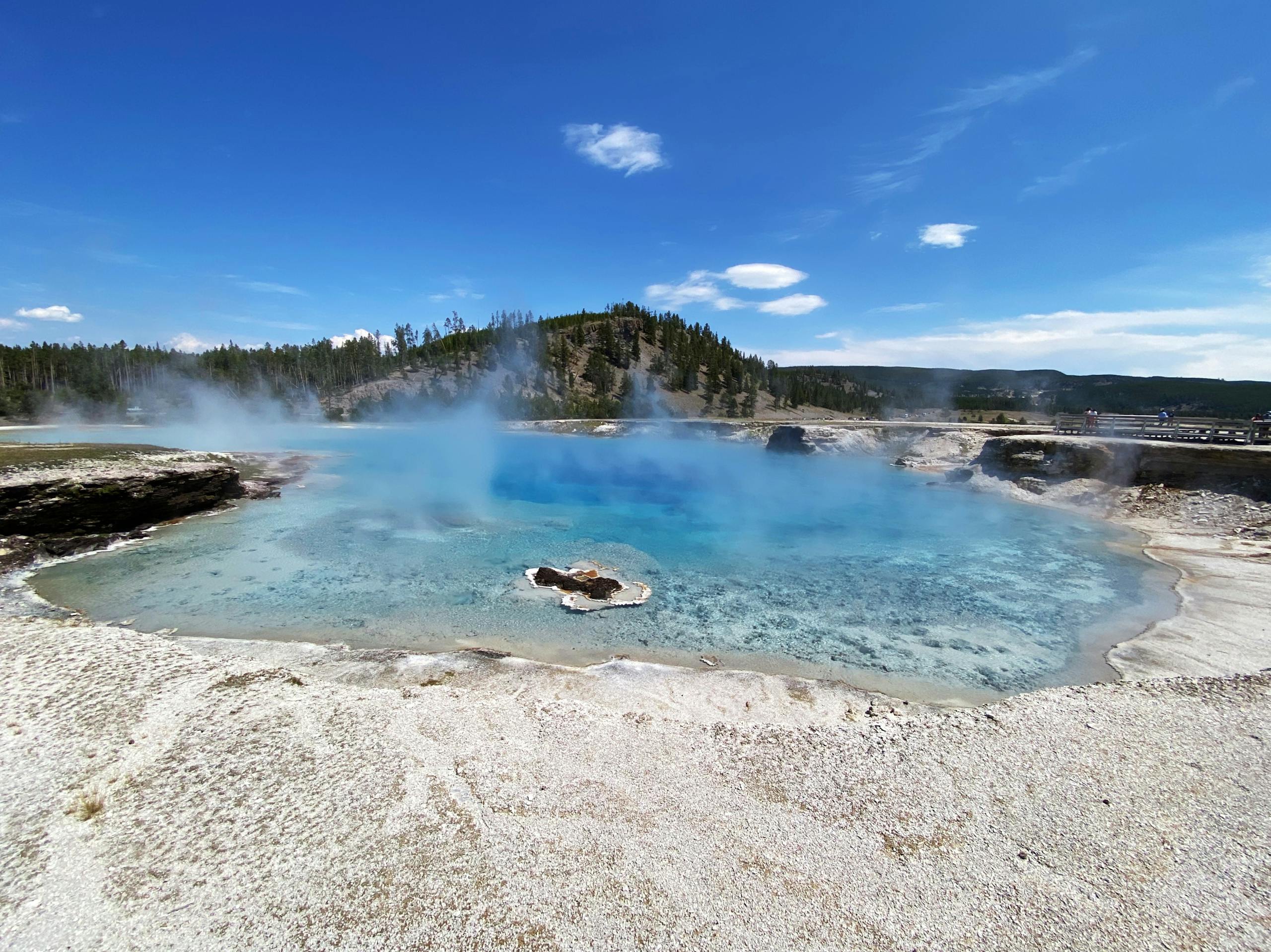Captivating blue geyser pool in Yellowstone National Park with steam under a clear blue sky.