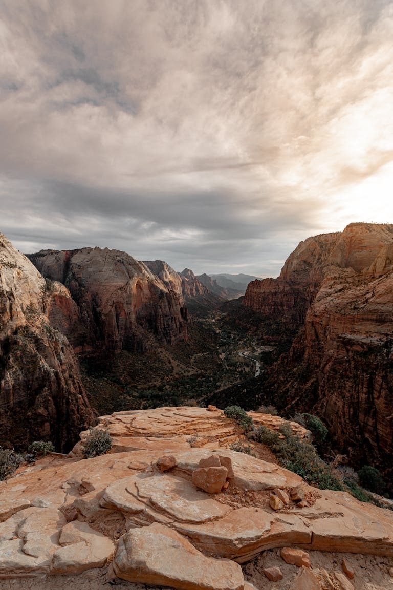 Capture of the dramatic Zion National Park cliffs on Canyon Overlook Trail during a tranquil sunset with a cloudy sky.