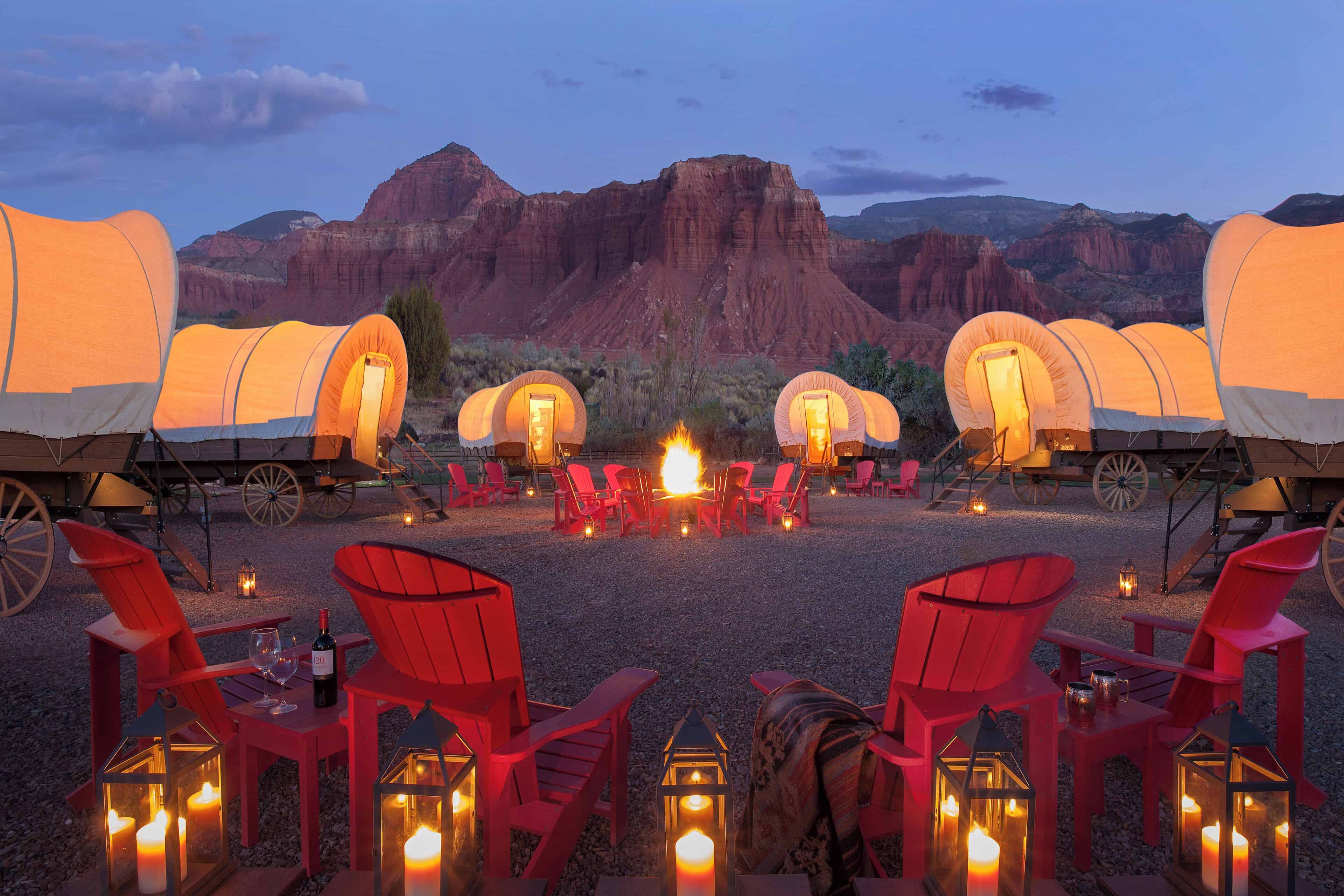 Covered wagons, fire pit and chairs with red mountains in the background outside of Capitol Reef Resort