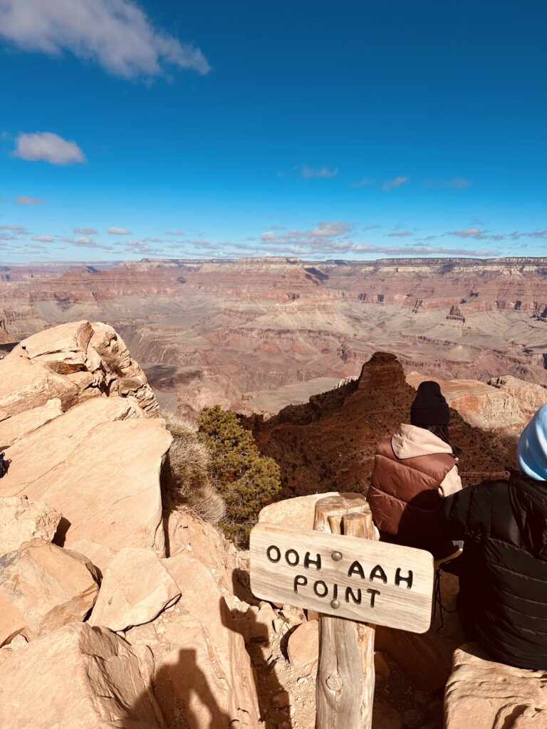 Hiker sitting next to the Ooh Aah Point sign on the South Kaibab Trail, enjoying the panoramic view of the Grand Canyon.