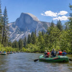 Family rafting on gentle scenic float on Merced River in Yosemite National Park with view of Half Dome