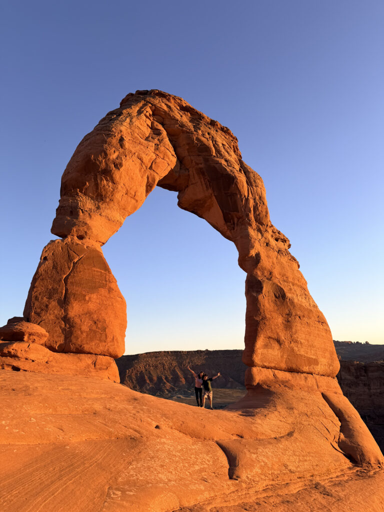 Delicate Arch at Arches National Park at sunset with woman and son under the arch