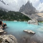Woman sitting at edge of turquoise water at Lago di Sorapis in the Dolomites, Italian Alps
