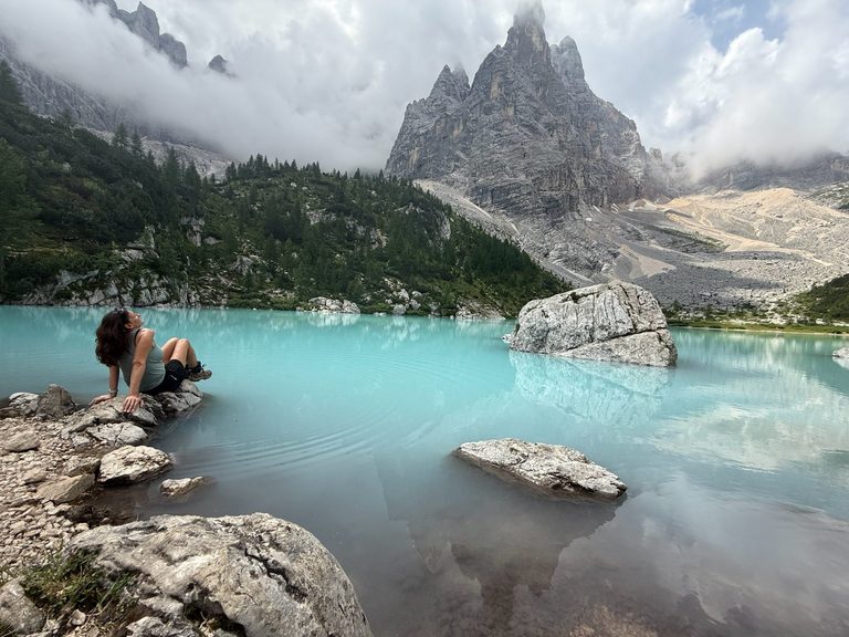 Woman sitting at edge of turquoise water at Lago di Sorapis in the Dolomites, Italian Alps