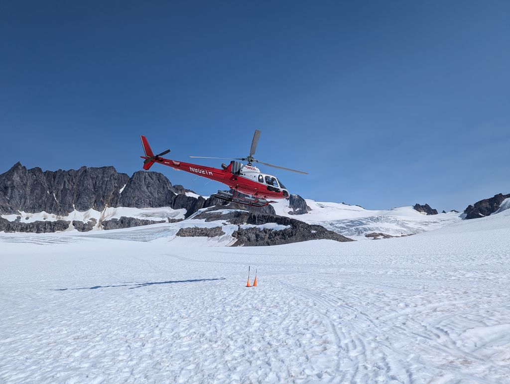 A red helicopter flies over a snowy glacier landscape in Skagway, Alaska.