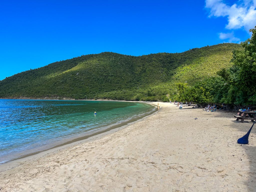 Serene beach scene in Cruz Bay, St John, featuring clear blue waters and lush green hills.